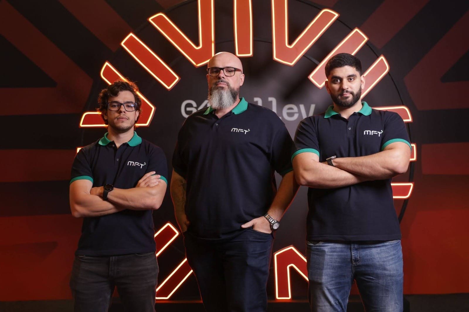 Equipe da MFT Inteligência: três profissionais com camisa polo preta e gola verde, de braços cruzados, em frente a um painel luminoso